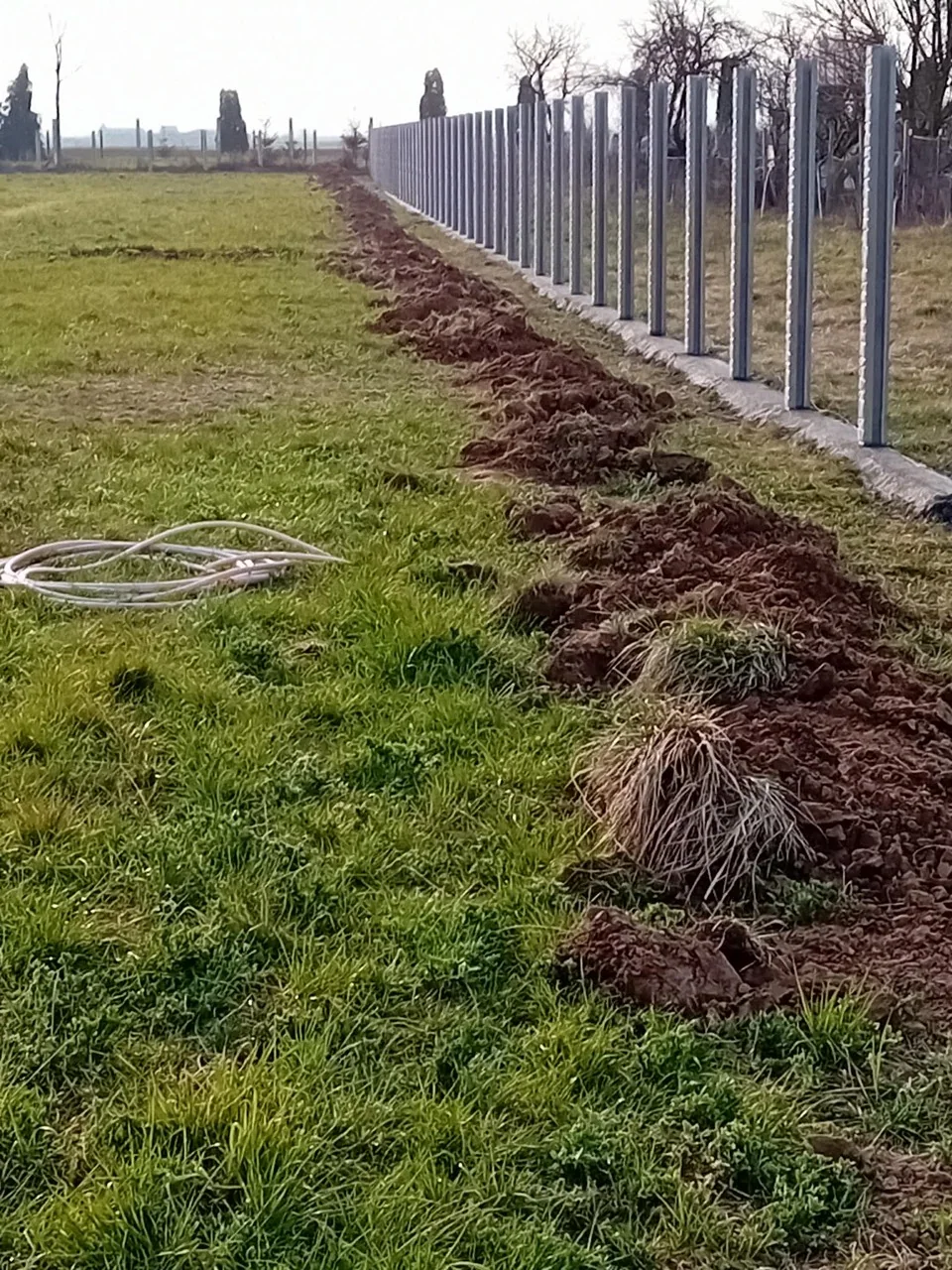 Șir lung de stâlpi prefabricați din beton montați pe fundație, înaintea panourilor, pe un teren deschis