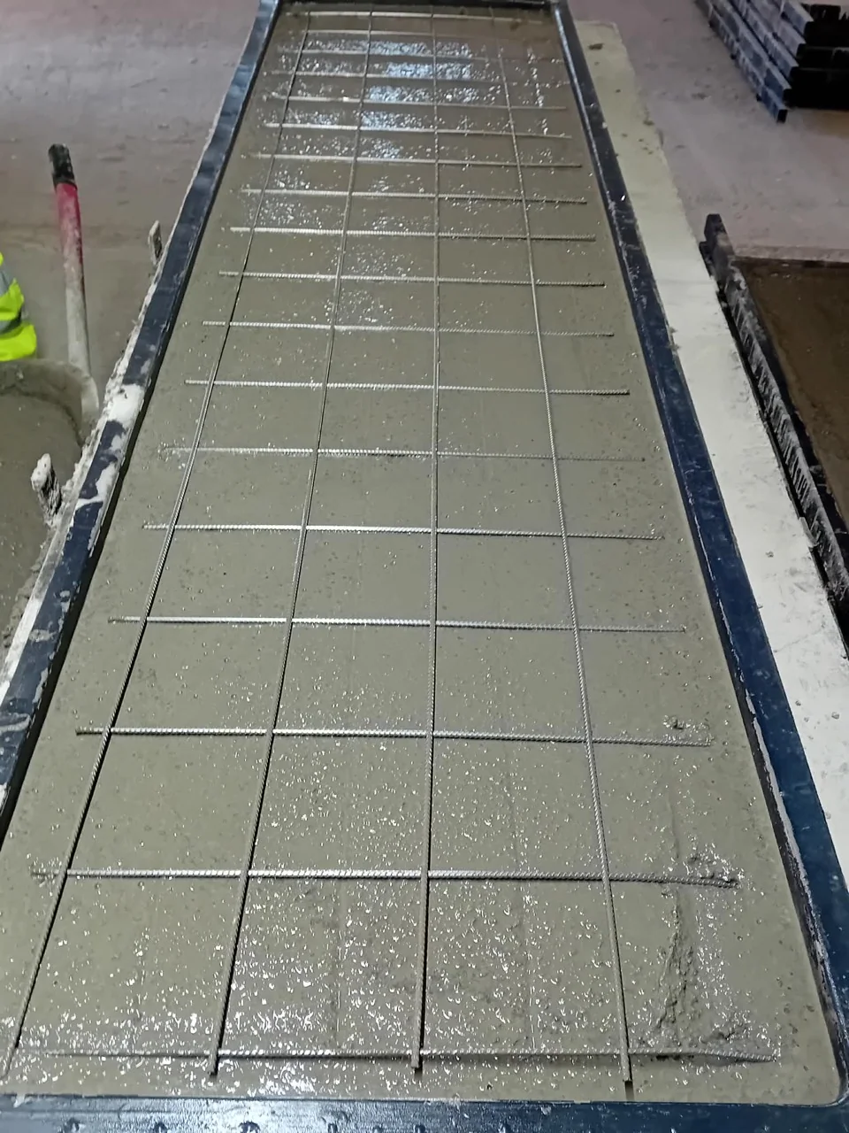 Beton proaspăt turnat într-o matriță pentru panou de gard, cu armătura metalică vizibilă