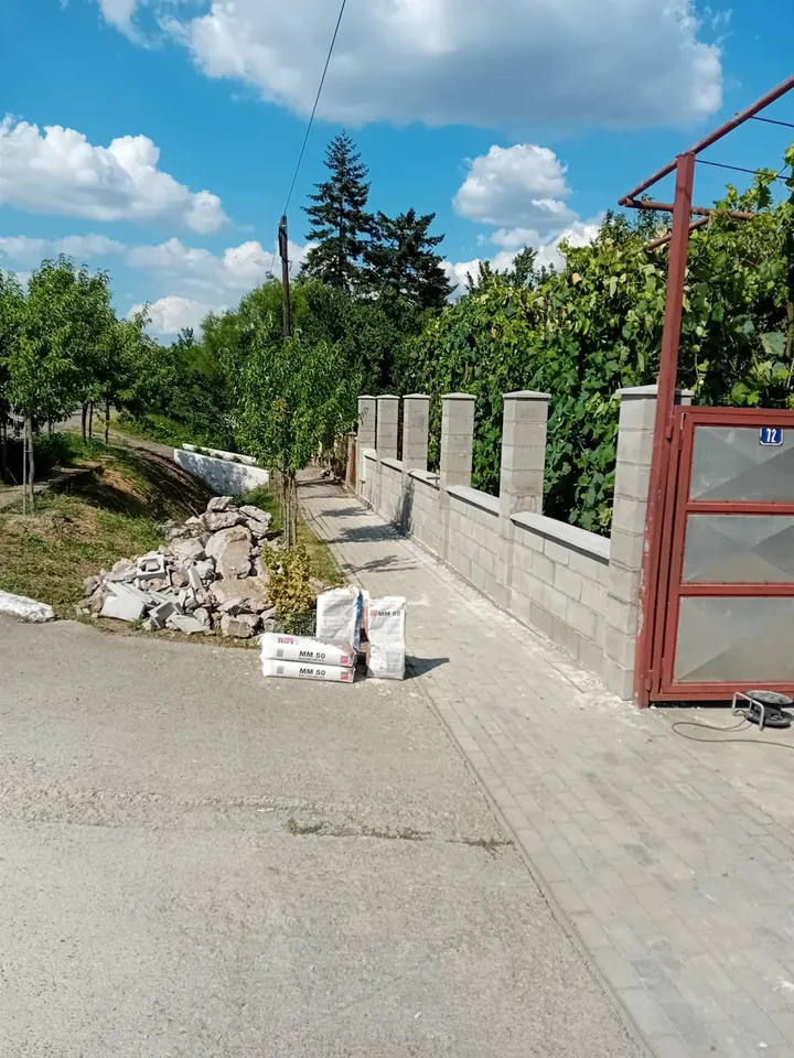 Gard din beton aproape finalizat, cu panouri, stâlpi și capace, lângă o poartă